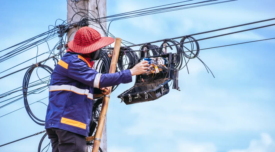Técnico de telecomunicaciones realizando mantenimiento en cables y equipos de red en un poste eléctrico al aire libre.